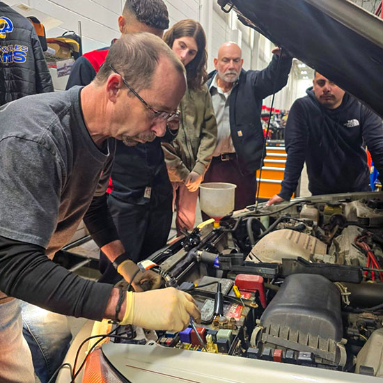 Mechanic working on vehicle engine while 4 people observe